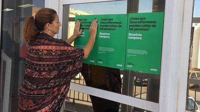 Una mujer coloca los carteles de la campaña a las puertas de un centro sanitario (CEDIDA) satse