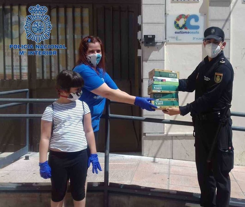 Un agente hace entrega de la donación de guantes a una responsable de Autismo-Ceuta (POLICÍA NACIONAL)