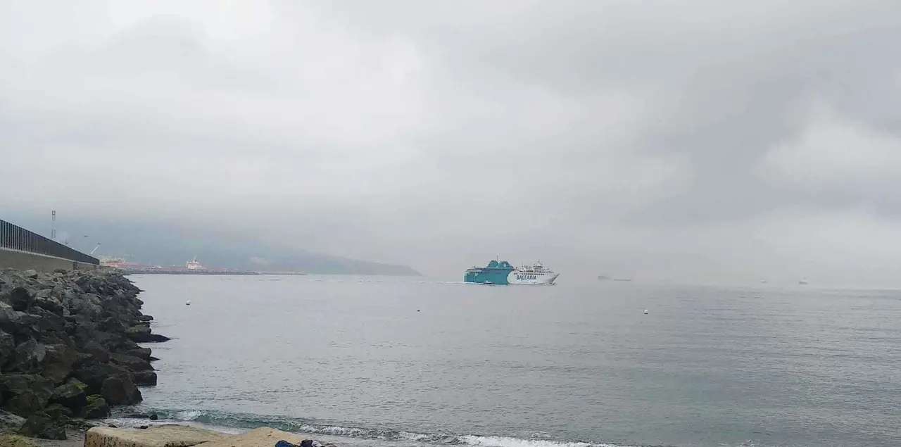 Playa de San Amaro con levante, cielos cubiertos. Al fondo, barco de Bale&agrave;ria.