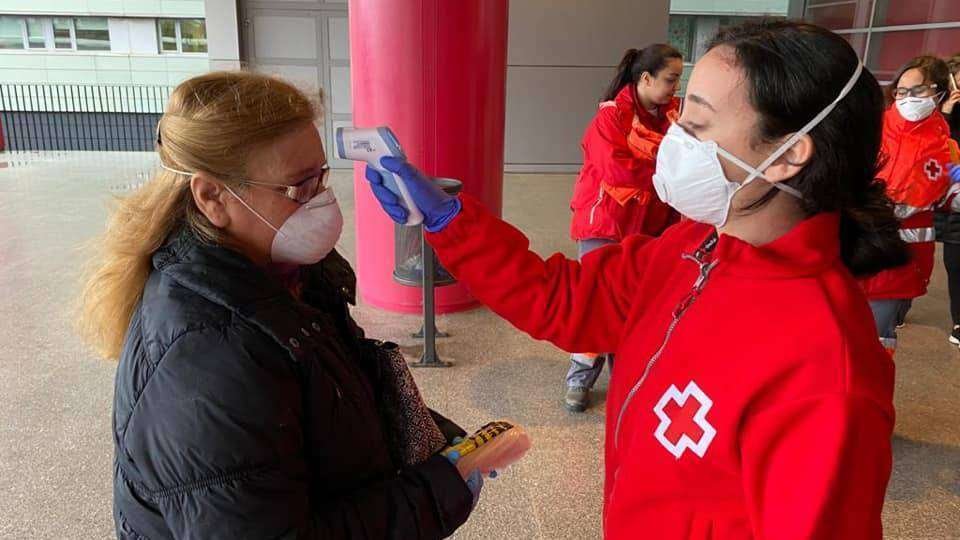 Una voluntaria de Cruz Roja toma la temperatura a una usuaria a la entrada de un centro sanitario (CRUZ ROJA)