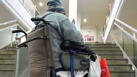 Una persona en silla de ruedas enfrentada al obst&aacute;culo de una escalera (C.A.)