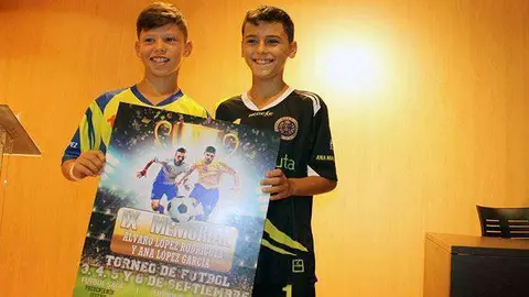 Dos j&oacute;venes jugadores muestran el cartel del IX Memorial (J. Ch.)