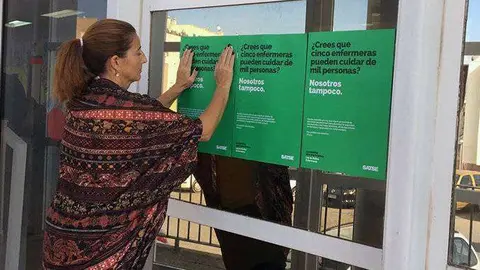 Una mujer coloca los carteles de la campa&ntilde;a a las puertas de un centro sanitario (CEDIDA) satse