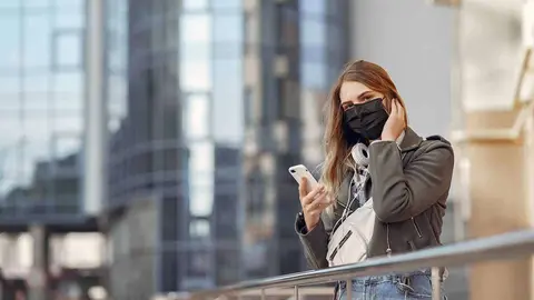 Woman in the city. Person in a mask. Coronavirus theme. Girl walks with phone and headphones.