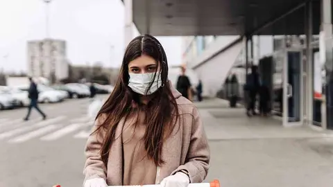 Young woman wearing protection face mask against coronavirus 2019-nCoV pushing a shopping cart. Concept of coronavirus