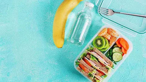 School lunch box with sandwich, vegetables, water, and fruits on table. Healthy eating habits concept. Flat lay. Top view